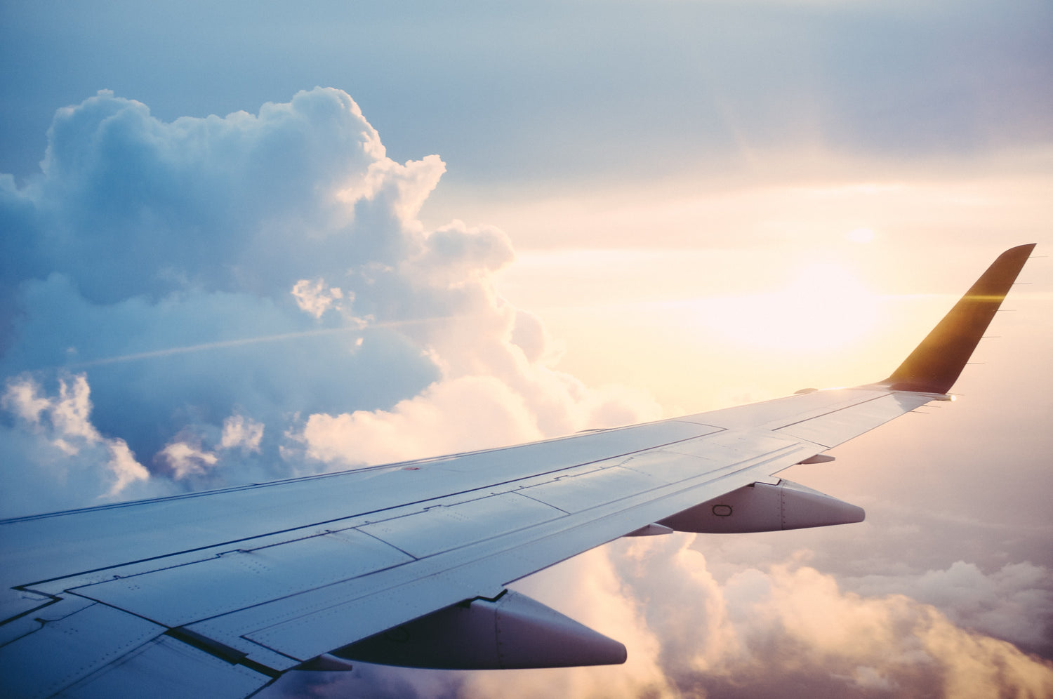 Wing of a plane with sky, clouds, sun in the background