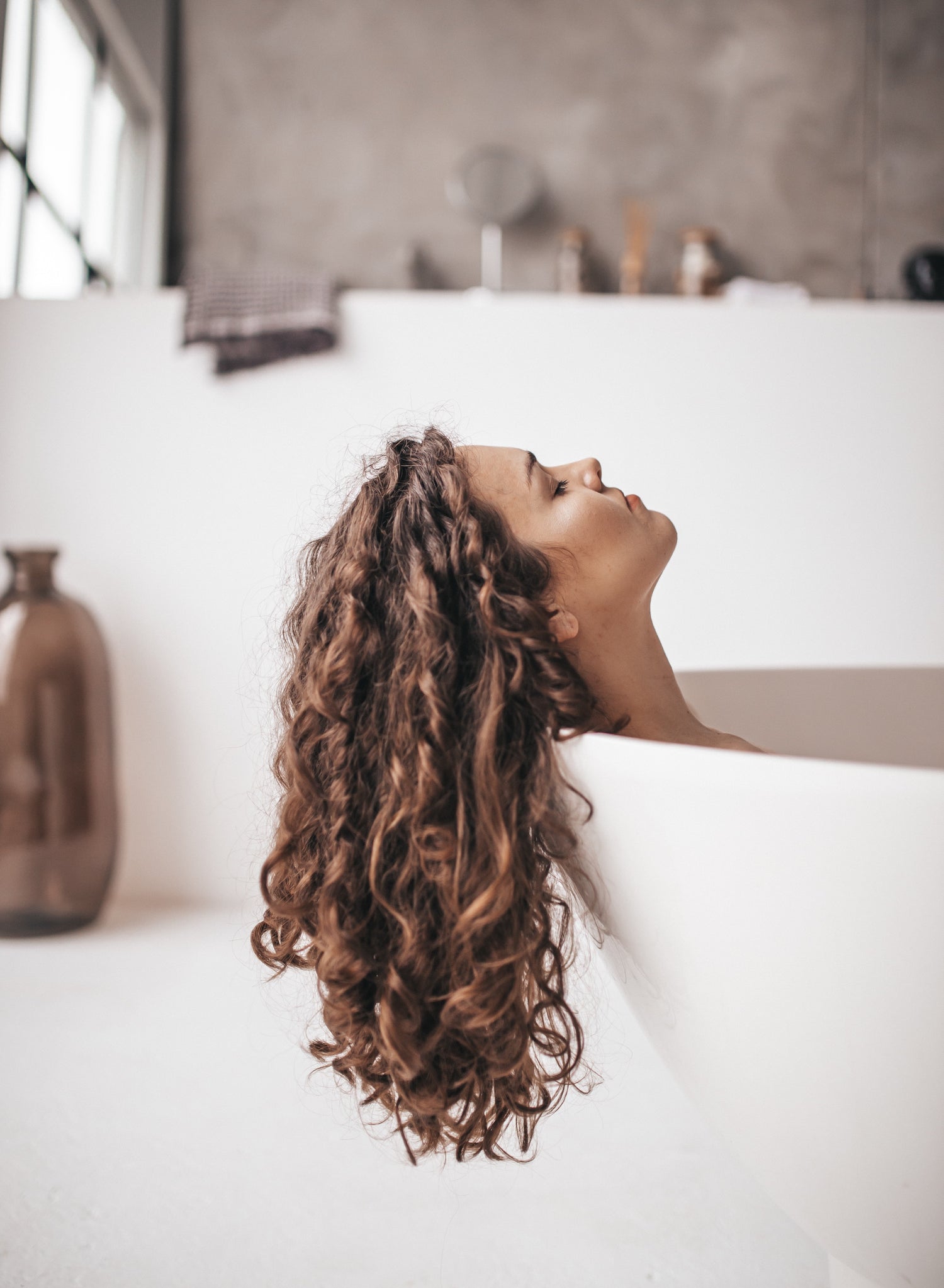 Woman in a tub with beautiful curly hair flowing over the edge